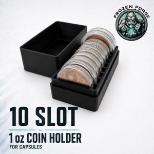 May include: A black 10-slot coin holder for capsules, featuring a rectangular base with ten vertical dividers and a separate matching lid. The holder contains several clear plastic capsules, each housing a copper-colored coin with a sun design.