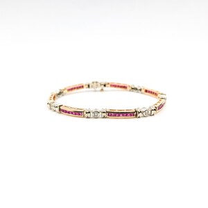 Pode incluir: Uma pulseira de ouro e prata com seções alternadas de pedras vermelhas retangulares e pequenos diamantes redondos. A pulseira é colocada em um fundo branco, destacando seu design intrincado e artesanato.