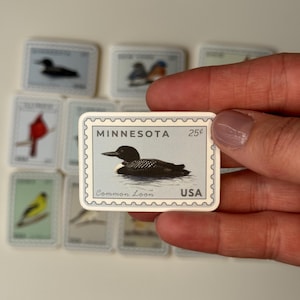 May include: A collection of miniature stamps featuring various birds. One stamp is in focus, displaying a Common Loon in water, with the text "MINNESOTA" and "USA". The stamps are in a rectangular shape with a white border.