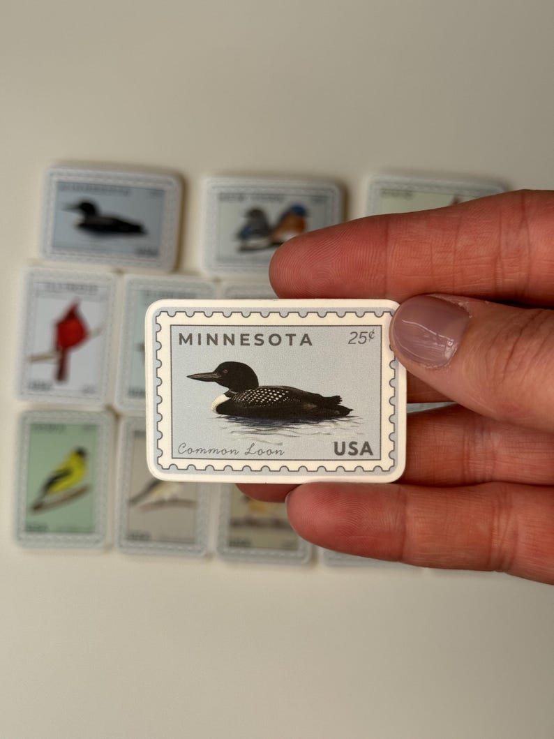 May include: A collection of miniature stamps featuring various birds. One stamp is in focus, displaying a Common Loon in water, with the text "MINNESOTA" and "USA". The stamps are in a rectangular shape with a white border.
