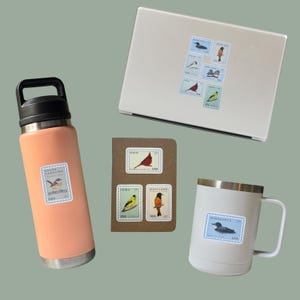 May include: An assortment of items featuring bird-themed stickers. A peach-colored water bottle, a white mug, and a laptop are adorned with stickers resembling vintage postage stamps. A small notebook displays similar stamps. The stickers showcase various bird illustrations.
