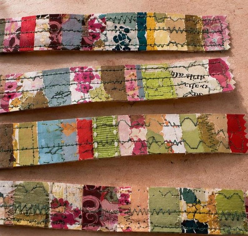 May include: Four horizontal strips of fabric featuring a patchwork design of various floral, solid, and patterned segments in shades of red, pink, yellow, green, and blue, all joined together with visible dark green zigzag machine stitching.