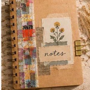 May include: A spiral-bound notebook with a tan cover featuring a vertical strip of colourful patterned paper, a rectangular collage element with a yellow flower illustration, and a torn paper label with the word notes written in black script.