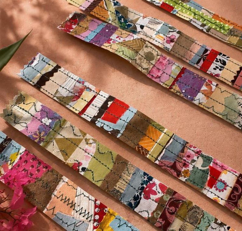 May include: Several long fabric strips featuring a patchwork of various colourful textile scraps in shades of red, pink, yellow, green, and blue. Each strip is reinforced with visible dark thread stitching in straight and zigzag patterns.