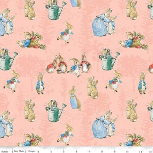 May include: A repeating pattern featuring illustrations of rabbits in various poses, watering cans, and bags of carrots on a light pink background. The design includes the text "Riley Blake Designs" and inch measurements.
