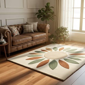 May include: A cream-coloured area rug with a large floral design. The flower has a beige centre and alternating green and brown petal shapes. The rug is placed on a hardwood floor in a living room setting.