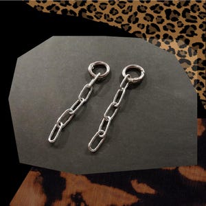 Könnte beinhalten: Ein Paar silberne Kettenohrringe mit einem Ringverschluss. Die Ketten bestehen aus kleinen, miteinander verbundenen Ovalen.