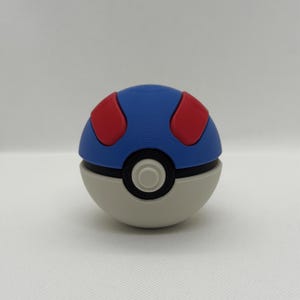 May include: A blue, red, and white Pok&eacute; Ball. The top half is blue with two red circular shapes. The bottom half is white with a black band and a white circle in the center.