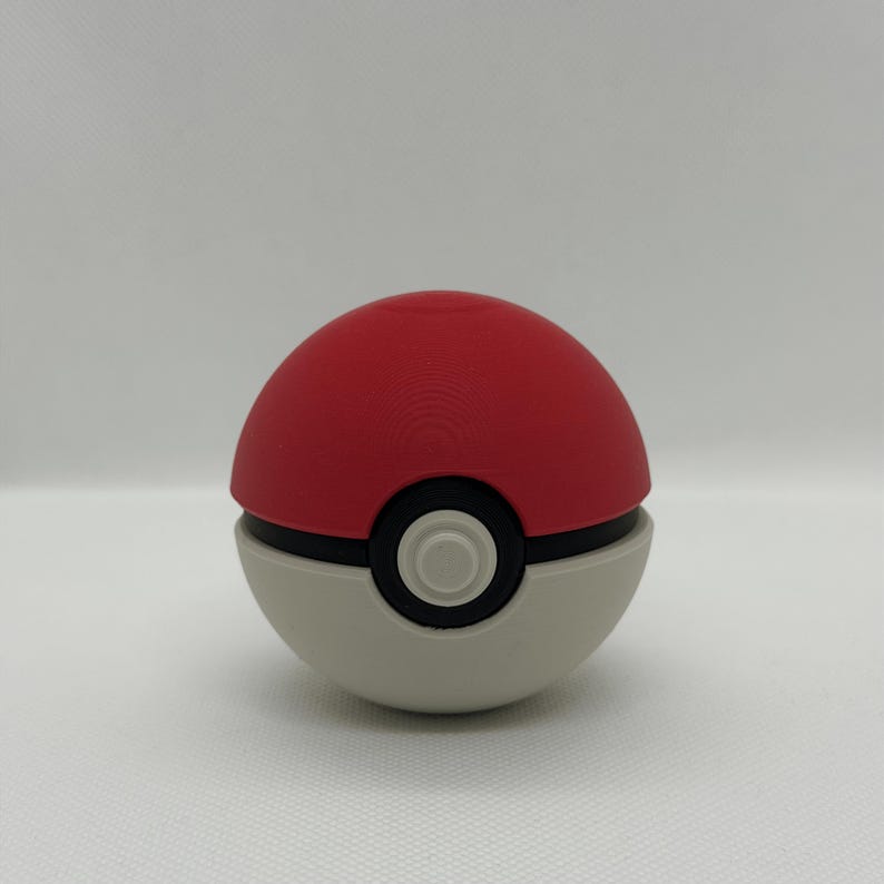 May include: A red and white Pok&eacute; Ball with a black band and a central button. The top half is red, the bottom half is white, and the button is black with a white center. A classic design.