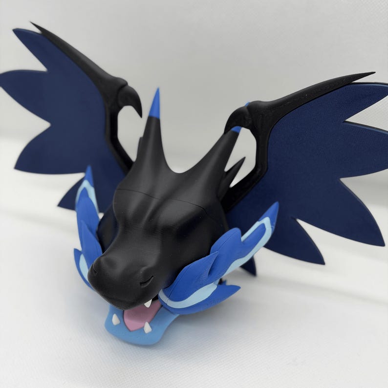 May include: A black and blue dragon head figurine with large wings. The figurine has a detailed design with blue accents on the wings and around the mouth. The dragon's mouth is open, revealing a pink interior.