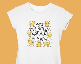 May include: White t-shirt featuring a playful graphic of yellow cartoon ducklings with the text "MOST DEFINITELY NOT ALL IN A ROW". The design includes stars and small green grass details, creating a whimsical and fun aesthetic.