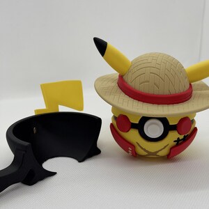 May include: A yellow Pikachu figure wearing a straw hat with a red band and black-rimmed glasses. The figure has red cheeks and a black lightning bolt tail. A black stand and a yellow lightning bolt are also present.