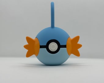 May include: A blue and orange cartoon-style character with a circular body, a vertical blue handle, and orange fin-like shapes on each side. The character has a black and white circular design in the center.