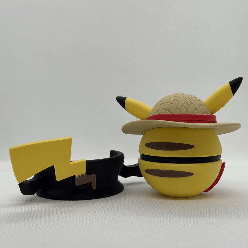 May include: A yellow Pikachu figure with a straw hat and a red band, and a black lightning bolt accessory. The figure has black-tipped ears and brown accents. The hat has a tan brim.
