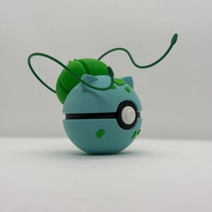 May include: A light blue and green spherical figurine with a black stripe and white button. The figurine has green accents and two green tendrils extending from the top. The figurine is a representation of a popular character.