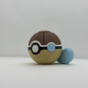 May include: A brown, tan, white, and blue novelty item, resembling a turtle. The item has a brown, segmented top, a tan base, and a white and blue circular design. A light blue turtle head and legs are attached.