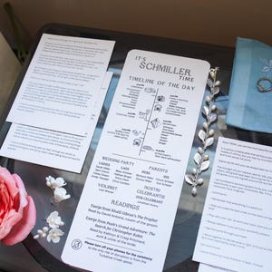 May include: A wedding timeline and details for the day, including the ceremony, cocktail hour, family photos, reception, and after party. The timeline is printed on a white card with black text and icons. The card is on a turntable with a floral arrangement and a pearl necklace.