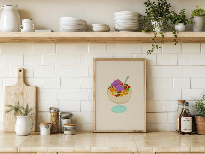 May include: A framed print of a colorful dessert in a glass bowl with a spoon. The dessert features purple ice cream, fruit, and other toppings. The print is displayed on a kitchen counter with other kitchen items.