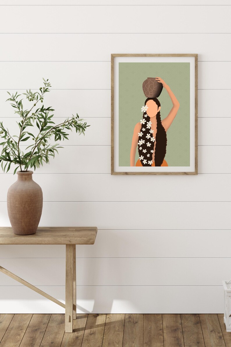 May include: Framed art print featuring a stylized illustration of a person with long, dark hair adorned with white flowers, balancing a brown pot on their head. The background is a muted green, and the frame is a natural wood color.