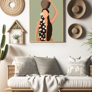 May include: A framed art print depicts a woman carrying a pot on her head, adorned with white flowers in her long, dark hair. The artwork is displayed above a white sofa with decorative pillows and a fringed throw, complemented by woven wall decor.