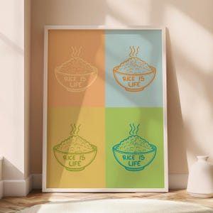 Puede incluir: Un póster enmarcado con cuatro cuadrados de colores. Cada cuadrado muestra un cuenco de arroz con vapor y el texto "RICE IS LIFE". Los colores de fondo son naranja, azul, verde amarillento y turquesa. La obra está en un marco blanco.