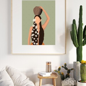 May include: Art print of a person carrying a brown pot on their head, with long dark hair adorned with white flowers. The artwork is framed and displayed on a white wall, with a wooden side table and cacti in the foreground.