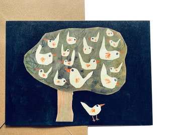 May include: A black card with a white tree and white birds on it. The tree has a brown trunk and green leaves. The birds are all facing the same direction. The card is on a brown envelope.