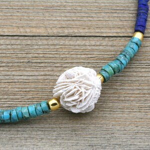 Puede incluir: Un collar de cuentas de coral blanco con cuentas turquesa y azules. El collar tiene un cierre dorado.