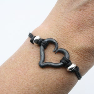 May include: A black leather bracelet with a silver heart charm and two silver beads.