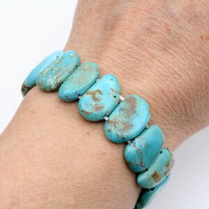 May include: Turquoise gemstone bracelet with a stretchy elastic band. The bracelet is made of smooth, oval-shaped stones with a light blue colour and brown marbling.