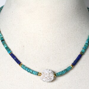 Puede incluir: Un collar de cuentas turquesa y azul con un colgante de concha blanca.