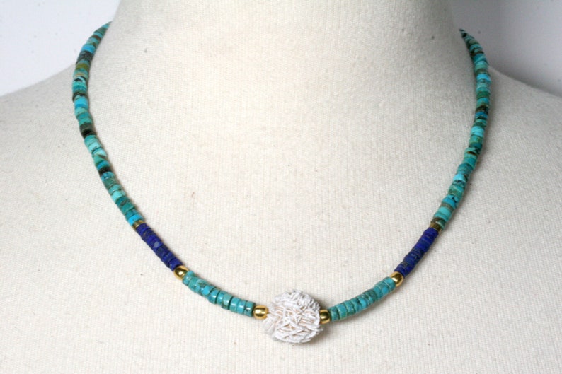 Puede incluir: Un collar de cuentas turquesa y azul con un colgante de concha blanca.