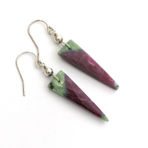 May include: A pair of silver earrings with green and pink gemstone drops. The gemstones are cut into a pointed shape.