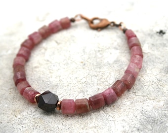 May include: A pink and copper bracelet with a dark gray gemstone. The bracelet is made of small, square-shaped beads.