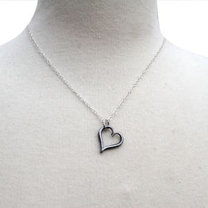 May include: A silver chain necklace with a silver heart pendant. The heart is open and has a delicate design.
