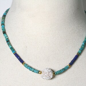 Puede incluir: Un collar de cuentas turquesa y azul con un colgante de concha blanca.