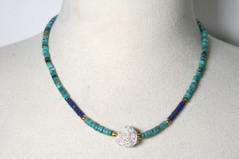 Puede incluir: Un collar de cuentas turquesa y azul con un colgante de concha blanca.
