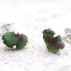 May include: A pair of silver stud earrings featuring green and pink rough gemstones.