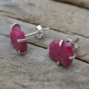 May include: A pair of silver earrings with pink ruby stones. The stones are rough and have a natural, unpolished look.