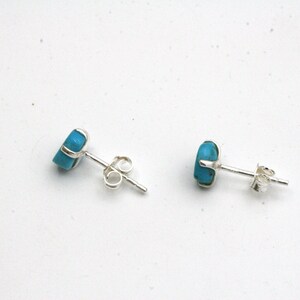 May include: A pair of silver stud earrings with turquoise stones. The earrings have a post and butterfly backing.
