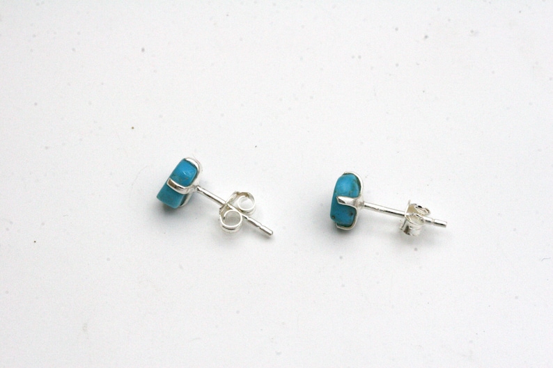 May include: A pair of silver stud earrings with turquoise stones. The earrings have a post and butterfly backing.