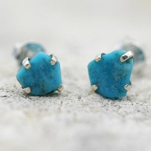 May include: A pair of silver stud earrings with turquoise stones. The stones are a light blue color and have a rough, natural texture.