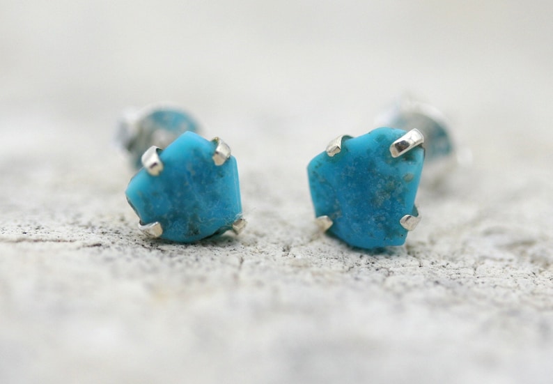 May include: A pair of silver stud earrings with turquoise stones. The stones are a light blue color and have a rough, natural texture.