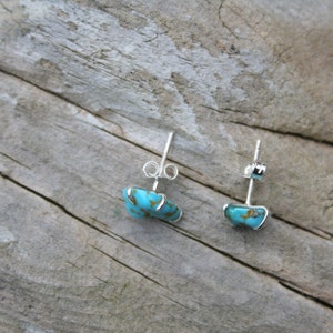 May include: A pair of silver earrings with turquoise stones. The stones are a light blue color with brown veins.