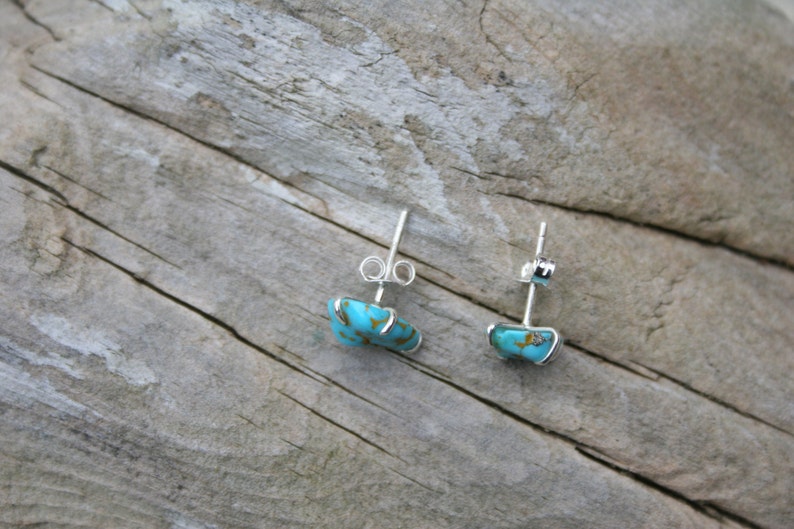 May include: A pair of silver earrings with turquoise stones. The stones are a light blue color with brown veins.