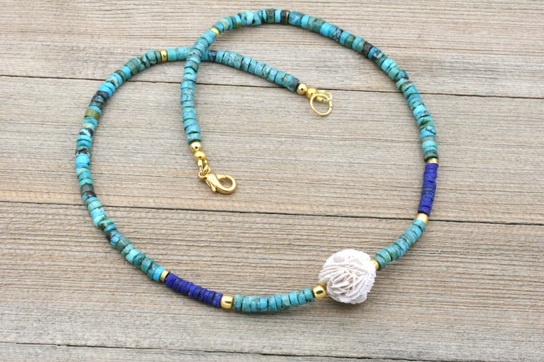 Puede incluir: Un collar de cuentas turquesa y azul con un colgante de concha blanca. El collar est&aacute; hecho con cuentas peque&ntilde;as y redondas y tiene un cierre dorado.