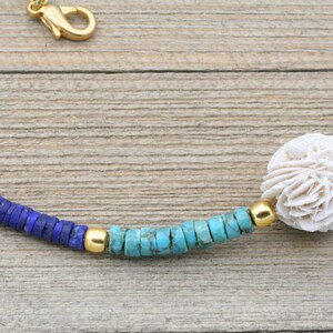Puede incluir: Un collar de cuentas turquesa, azul y dorado con una pieza central de coral blanco.