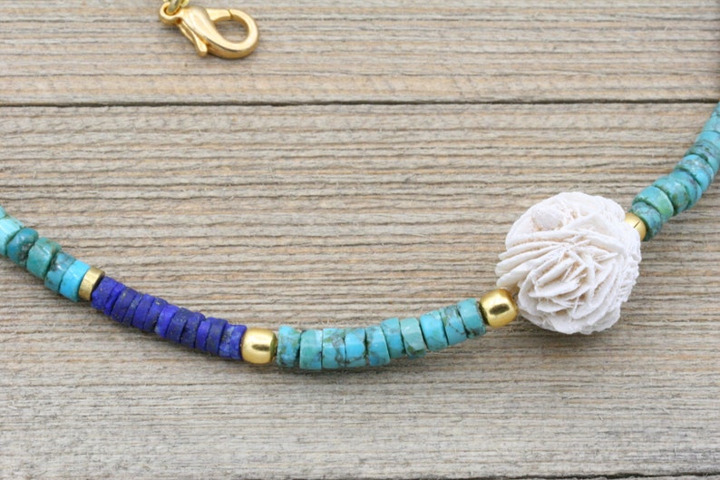 Puede incluir: Un collar de cuentas turquesa, azul y dorado con una pieza central de coral blanco.