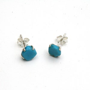 May include: A pair of silver stud earrings with turquoise stones. The stones are a bright blue color and are set in a silver bezel.