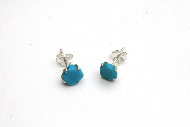 May include: A pair of silver stud earrings with turquoise stones. The stones are a bright blue color and are set in a silver bezel.